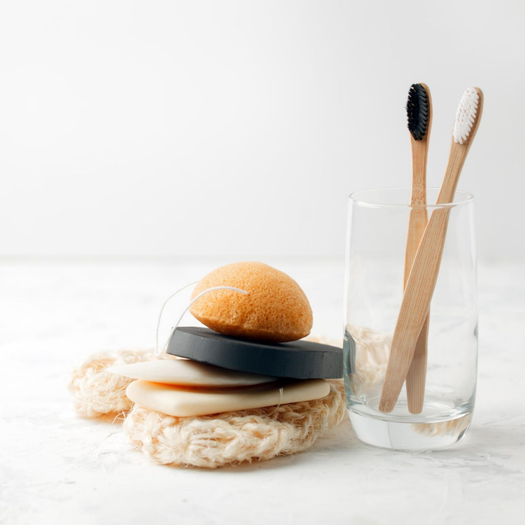 Pure Skin Natural Living Collection- A collection of natural soaps, a sponge, loofah, next to two wooden tooth brushes in a glass.