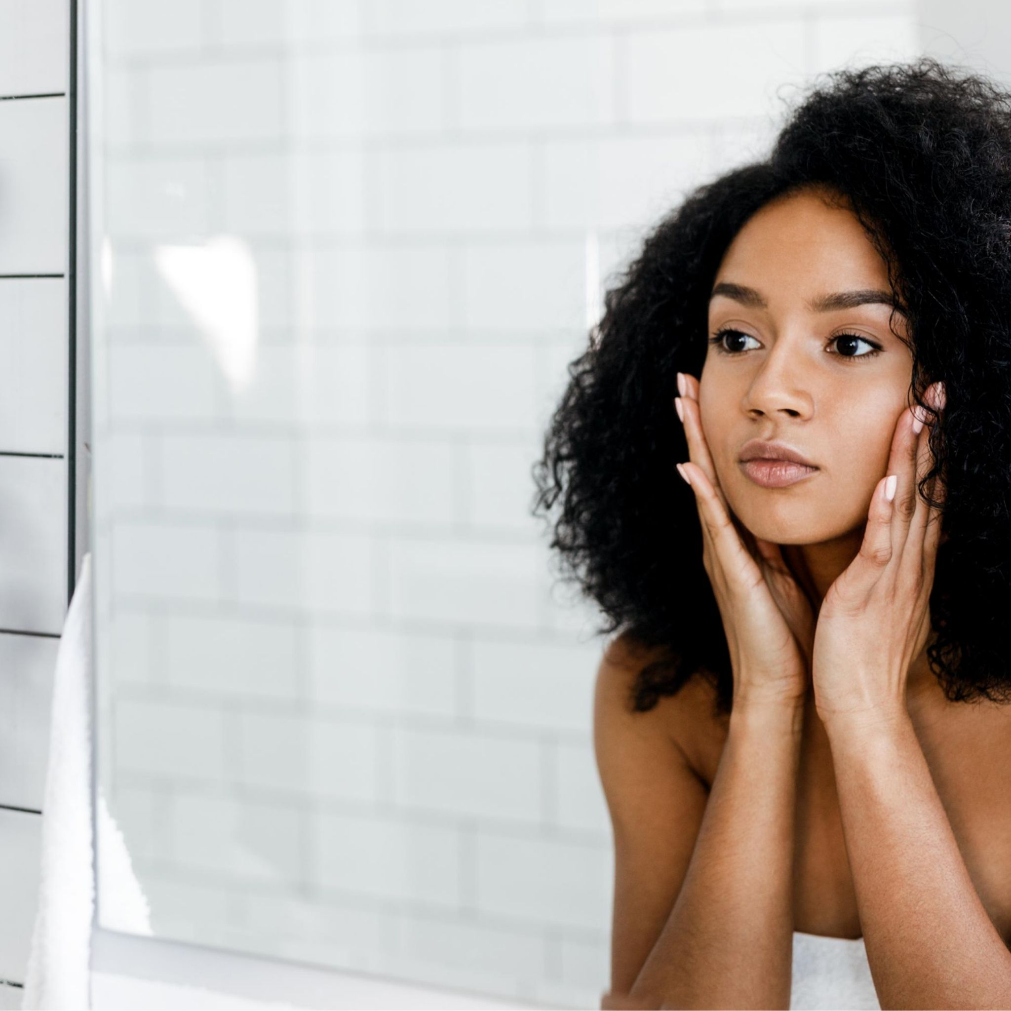 Pure Skin Face Care Collection- A woman touching her face while looking into a mirror at herself.